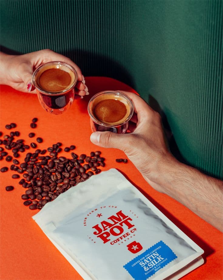 Hands holding espresso shots above coffee beans with green background
